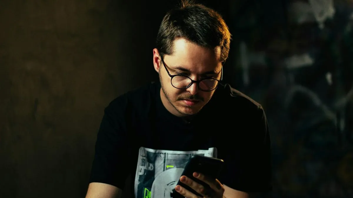 A man with glasses and a black t-shirt looking intently at his smartphone.