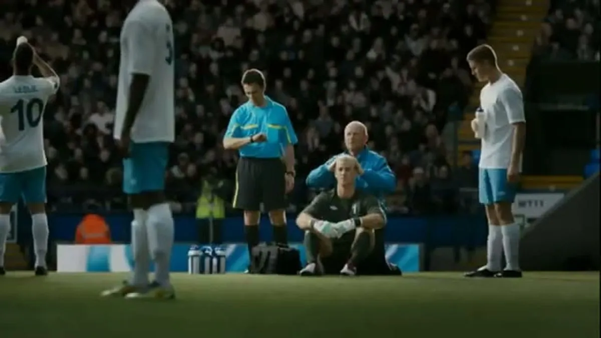 A wide shot of a football pitch with several players, a referee, and a coach tending to a player.