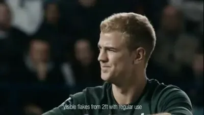 Joe Hart, a male footballer with short blonde hair, looks to the right, smiling slightly, on a football pitch.