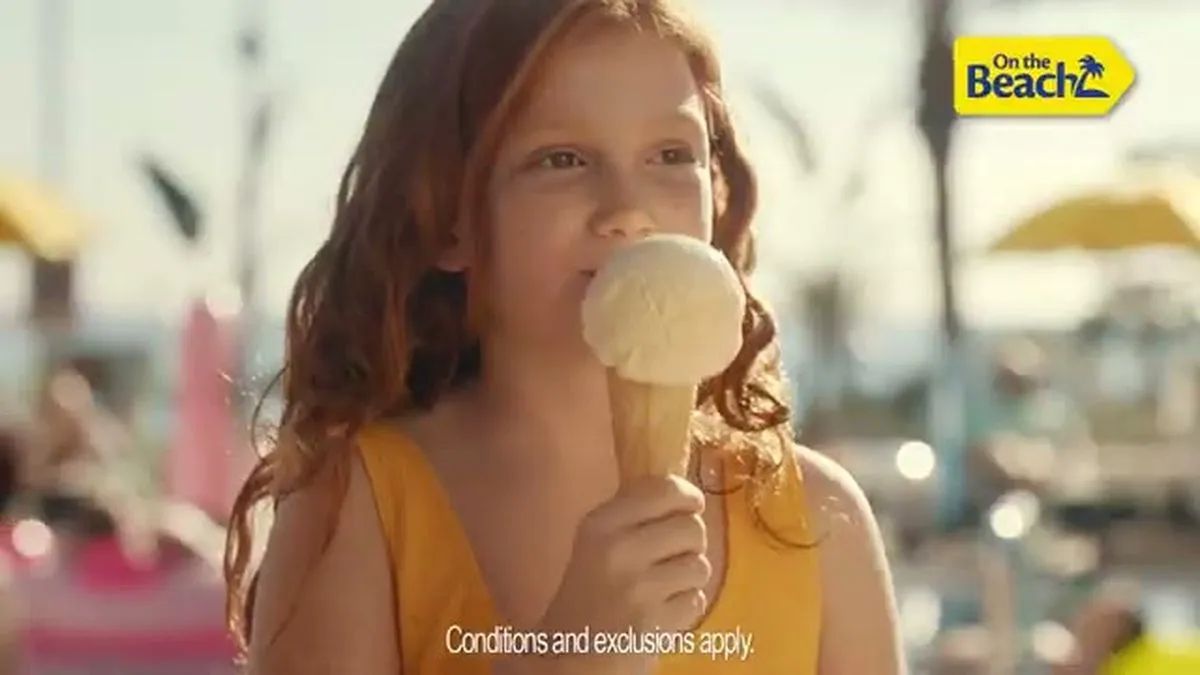 A young girl with long red hair eats an ice cream cone, looking towards the right.