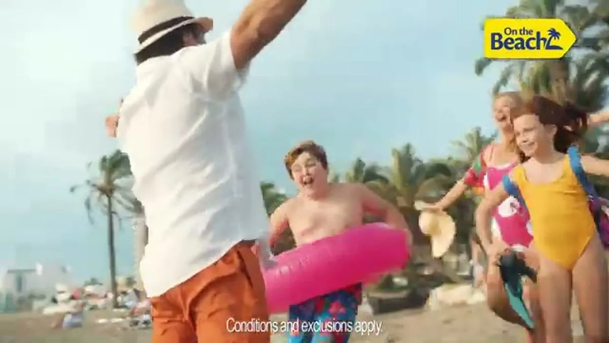 A family, including a man in a hat, a woman, and two children, runs joyfully towards the camera on a beach.