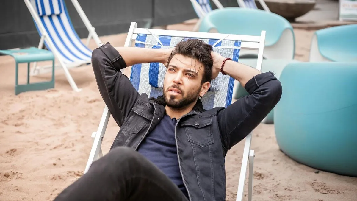 A man with a beard relaxing in a striped beach chair on a sandy beach.