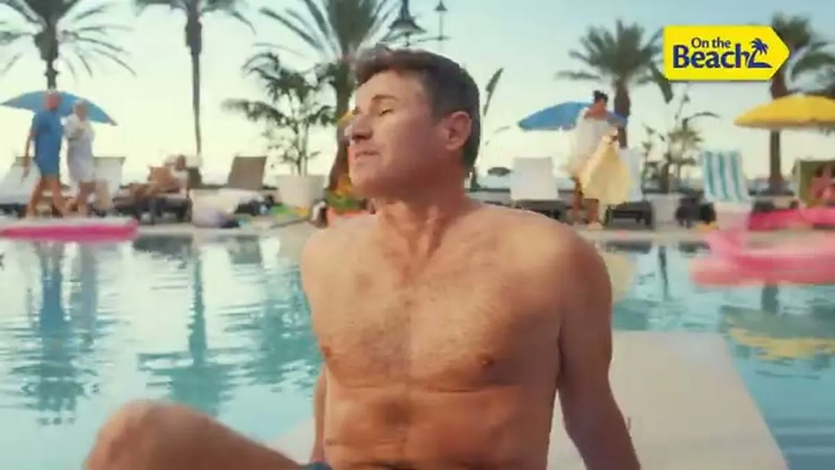 Paddy McGuinness, a man with short brown hair and a hairy chest, sits by a pool, looking relaxed.