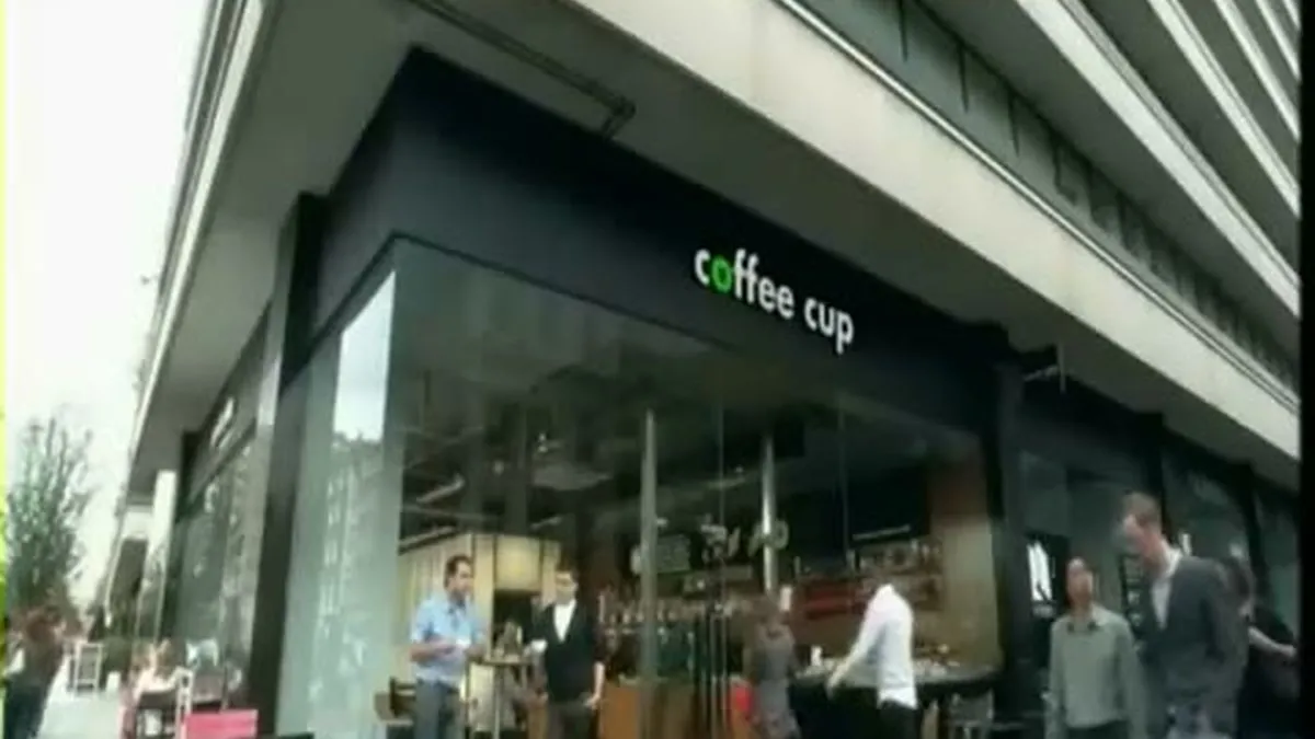 An exterior wide shot of a modern coffee shop called 'coffee cup' with people sitting outside and inside.