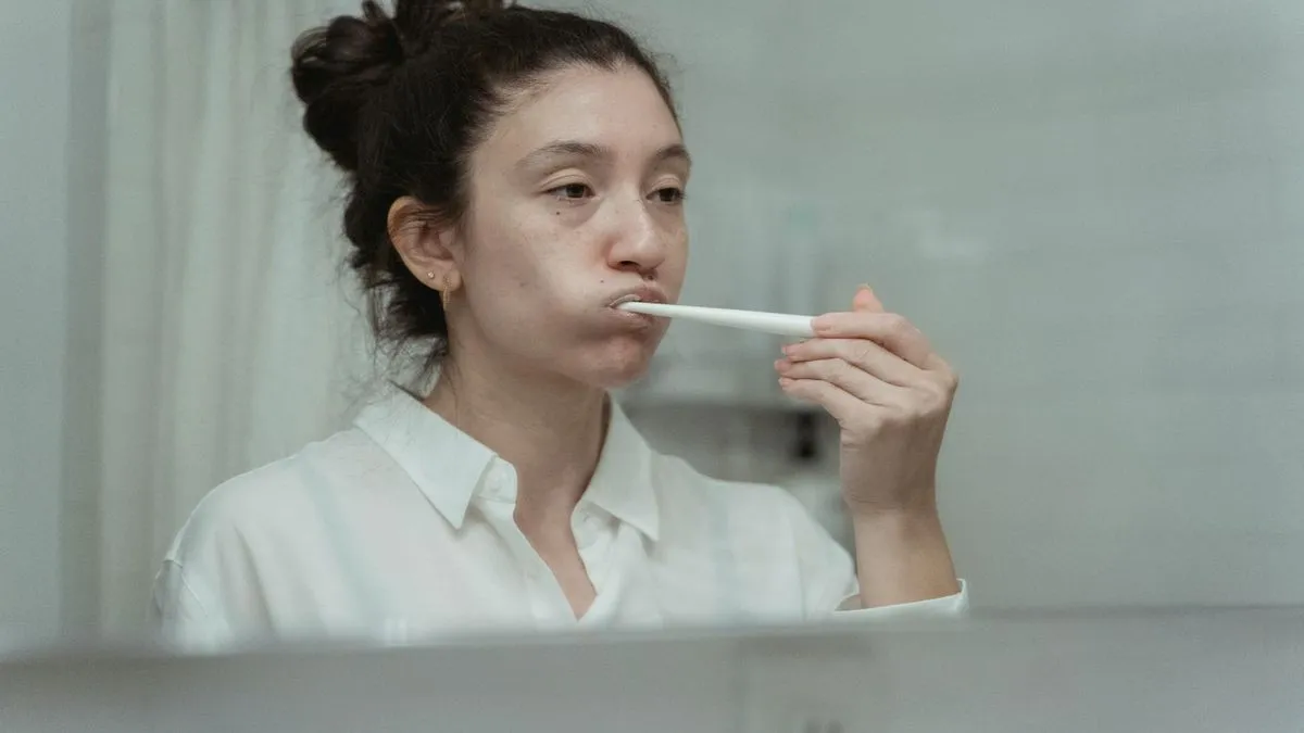 A woman with her hair tied up brushing her teeth in front of a mirror.