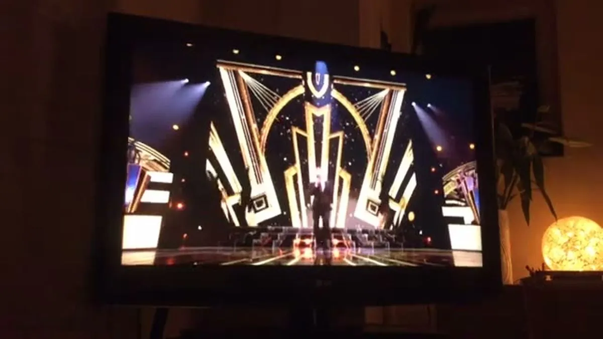 A wide shot of a brightly lit stage with a large, ornate gold and black geometric backdrop, ready for a performance.