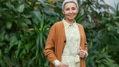 A smiling older woman with short grey hair wearing a brown cardigan and patterned shirt.