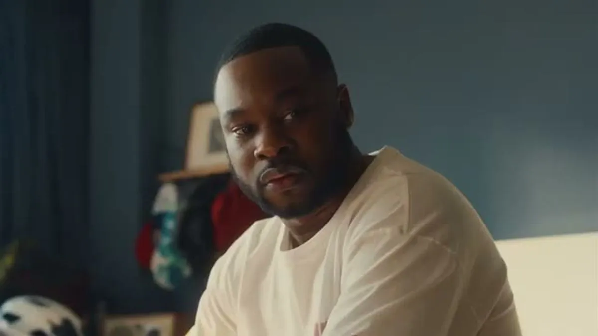 A man with a beard and white t-shirt looks directly at the camera.
