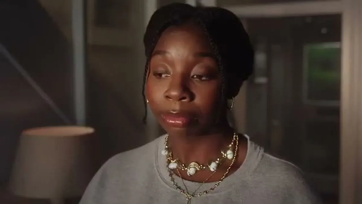 A young Black woman with a pearl necklace looks slightly upwards.