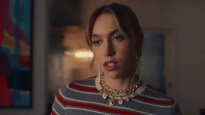 A young woman with blonde hair and a gold necklace looks slightly to the right.