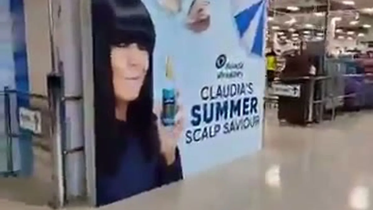 A wide shot of a Sainsbury's UK store aisle with a Head & Shoulders display featuring Claudia Winkleman.