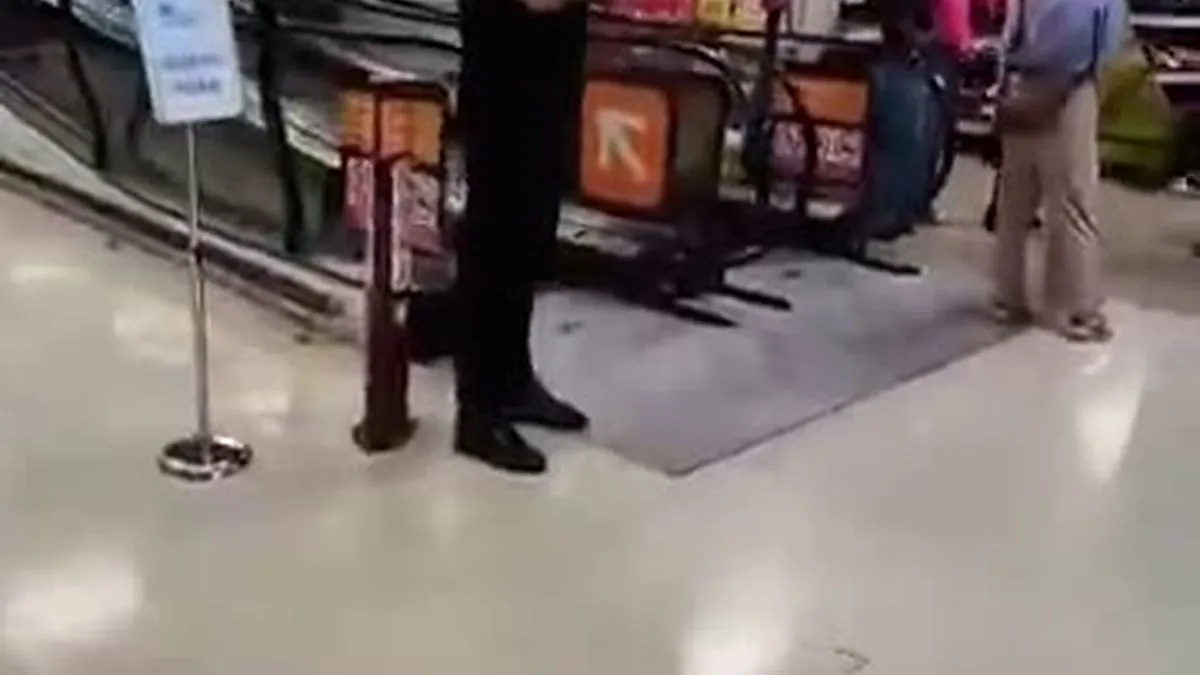 A man in a black shirt and trousers stands in a Sainsbury's UK store, looking to the right.