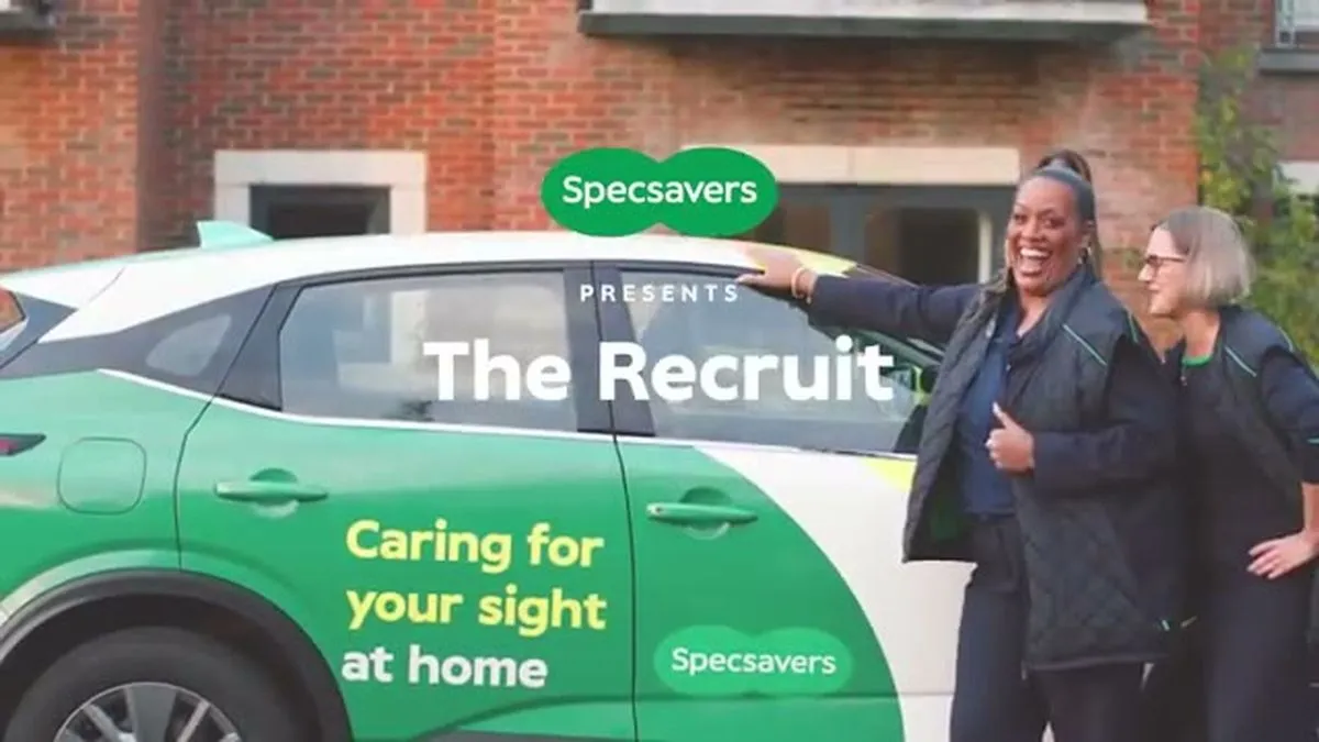 Alison Hammond and Julie stand smiling next to a Specsavers branded car outside a building.