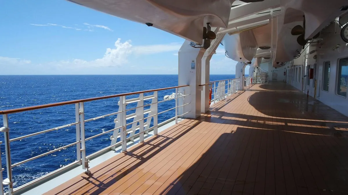 A cruise ship deck with a wooden floor and white railings overlooking the blue ocean.