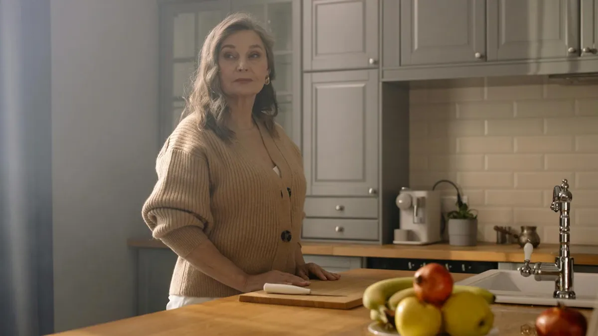 Elegant elderly woman in a cozy kitchen setting with natural lighting and a bowl of fresh fruit.