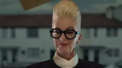 Aunt Helga, a woman with a tall blonde beehive and large round glasses, smiles at the camera.