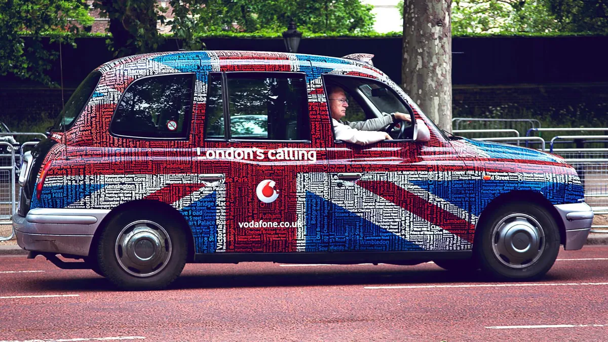 A vibrant Union Jack styled London taxi driving through central London.