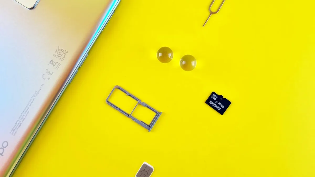 Close-up of a mobile phone with a SIM card, SIM tray, and memory card on a vibrant yellow surface.