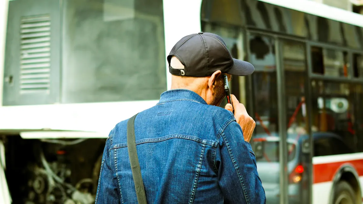A man in a cap examines a broken-down bus on a city street.